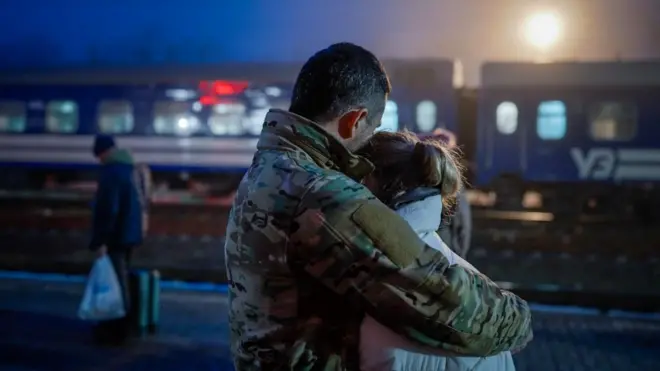 Un hombre en uniforme abraza a una mujer en una estación de tren. 