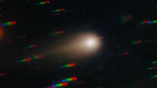 دنباله‌دار اطلس ۳‌آی به صورت یک نقطه درخشان که توسط یک هاله (کُما) مه‌آلود و دمی که در سمت چپ آن قرار دارد، نمایش داده شده است؛ در پس‌زمینه، خطوطی از نقاط آبی، سبز و قرمز دیده می‌شوند که نشان‌دهنده ستارگانی هستند که نسبت به دنباله‌دار در حال حرکتند.