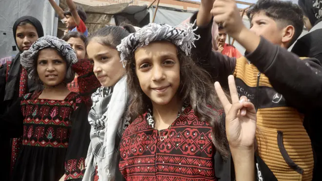 Niños palestinos reunidos en una celebración tras el anuncio de cese al fuego. Una de ellos, en el medio del plano, posa ante la cámara haciendo con sus dedos el símbolo de la paz.