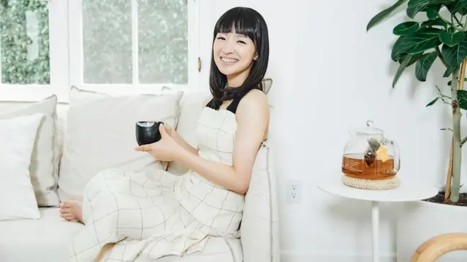 Marie Kondo sentada no sofá com xícaracasino bonus no cadastrochá na mão