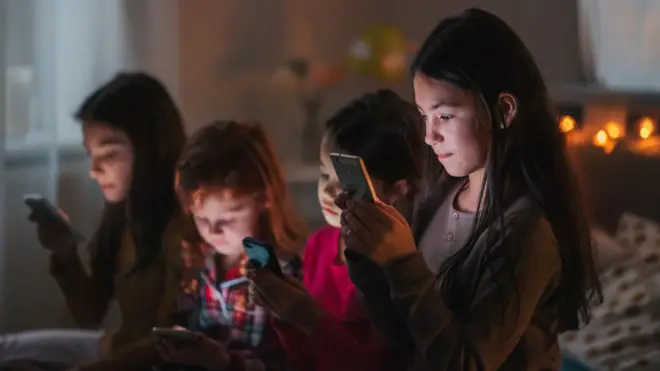 Un grupo de niñas mira sus teléfonos celulares.