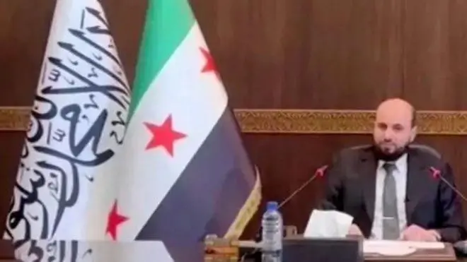 या फोटोत सीरियाच्या हंगामी पंतप्रधानांच्या बैठकीत पांढरा झेंडा दिसत आहे.