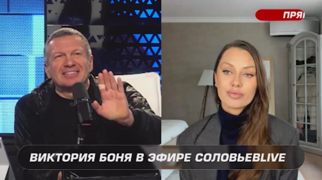 Скриншот из эфира, на одной половине улыбается Владимир Соловьев, поднося руку (на указательном пальце — пластырь) к микрофону, на другой половине Виктория Боня. 