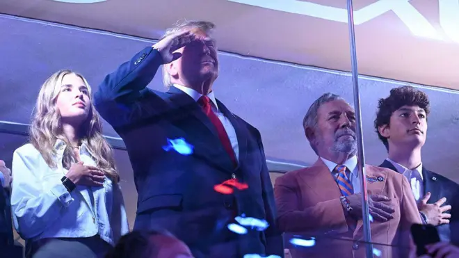 Trump, torunu ve Knick yöneticisiyle birlikte tribünde selam veriyor.