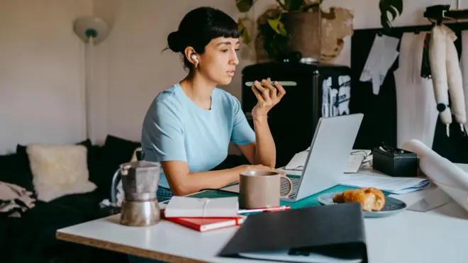 Девојка прича на телефон, испред њен је лаптоп