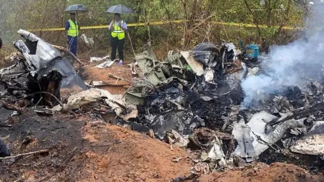 Two people with umbrellas and high-viz jackets are seen at the wreckage of the aircraft in Kwale County, Kenya