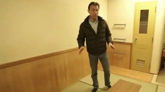 たたみの狭い部屋に立つBBC記者

