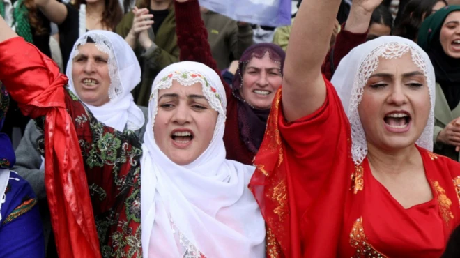 Dört beyaz yemeni giymiş kadın slogan atıyor gibi görünüyor. Renkli elbiseler giymişler ve güçlü görünüyorlar..