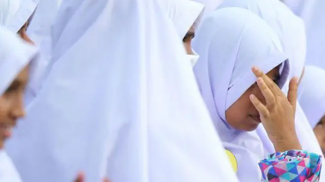 සුදු පැහැති මුස්ලිම් ආගමික ඇඳුම් වලින් සැරසී සිටින පාසල් දැරියක් පිරිසක්