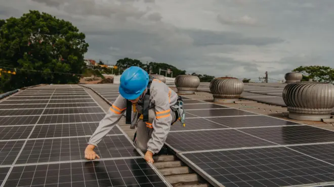 Mulher de uniforme e capacete trabalhando na instalação de painéis solares