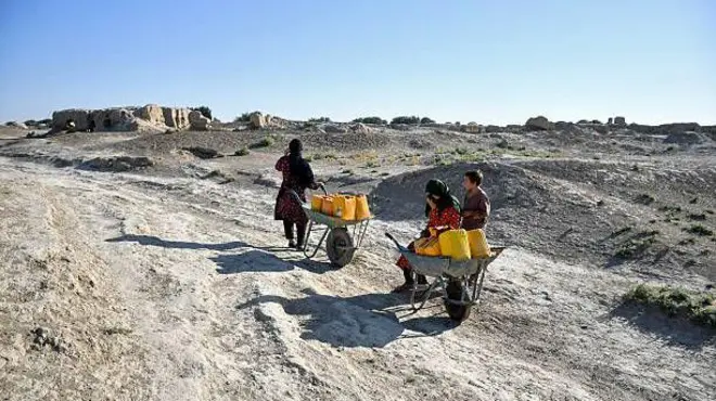 تصویر دو کودک و یک زن که با استفاده از کراچی و بشکه‌ها آب را به خانه‌های شان انتقال می‌دهند. افغانستان در سال گذشته شاهد خشک‌سالی و کمبود آب بود. 