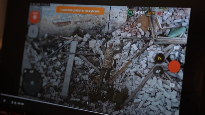 Bir drone görüntüsünde ellerini kaldırmış bir asker yıkıntılar arasında yürüyor.