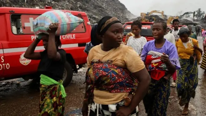 Akitan kan ga gogoro ninu aworan yii, bẹẹ ni awọn obinrin kan n fi ẹṣẹ rin lọ, awọn kan pọn ọmọ sẹyin ninu wọn, bẹẹ ni ẹnikan gbe apo ru sori.
 Ẹrọ katkata wa lẹyin, bẹẹ ni ọkọ pupa kan naa wa nibẹ pẹlu.