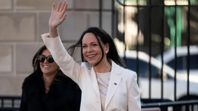 Beyaz bir elbise giymiş María Corina Machado, Beyaz Saray'dan ayrıldıktan sonra el sallıyor.