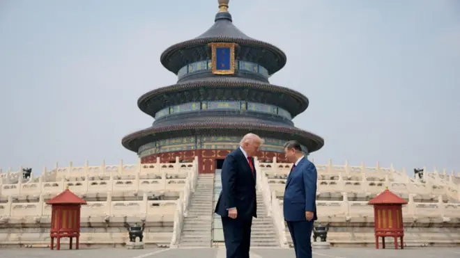 Los presidentes Trump y Xi permanecen de pie, uno frente al otro y con la cabeza ligeramente inclinada, ante unos escalones ornamentados que conducen a un grandioso templo chino de tres niveles, en tonos azules, verdes, rojos y dorados.