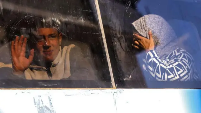 سيدة محجبة في باص تبكي، وأمامها شاب يلوح بيده أثناء توجههم لمعبر رفح