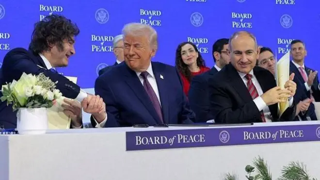 Дональд Трамп, який заснував нову міжнародну організацію, сидить за столом і тисне руки іншим учасникам зібрання.