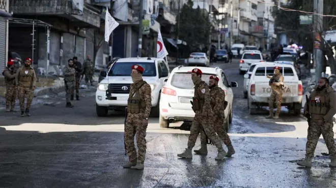 Suriye'nin askeri polis mensupları bir sokakta yürüyüş yapıyor. Arka planda araçlar var. 