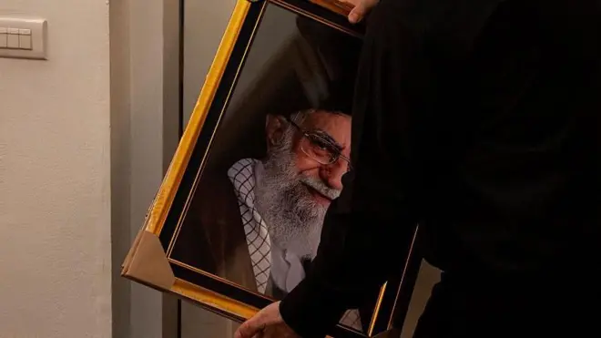 یک مرد که از پشت سر دیدهمی شود قاب عکس علی خامنهای را در دست دارد.