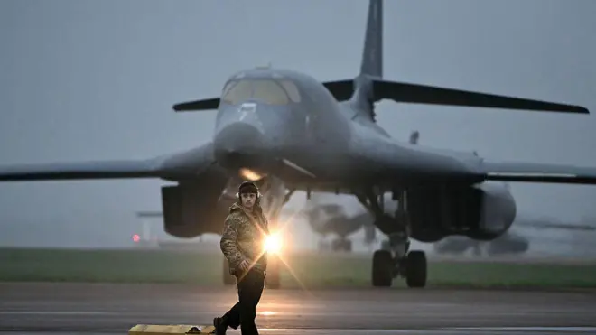 7 मार्च 2026 को सूर्योदय के तुरंत बाद दक्षिण-पश्चिम इंग्लैंड के RAF फ़ेयरफ़ोर्ड एयरबेस पर अमेरिकी वायुसेना के B-1 लांसर बॉम्बर के सामने एक ग्राउंड क्रू सदस्य खड़ा है. ब्रिटेन के प्रधानमंत्री किएर स्टार्मर ने वॉशिंगटन को हिंद महासागर में स्थित डिएगो गार्सिया और दक्षिण-पश्चिम इंग्लैंड के RAF फ़ेयरफ़ोर्ड एयरबेस का इस्तेमाल ईरान के मिसाइल ठिकानों पर बमबारी करने के लिए करने की मंज़ूरी दे दी है. यह फैसला तब लिया गया जब ईरान की जवाबी कार्रवाइयों में खाड़ी के कई देशों को निशाना बनाया गया.