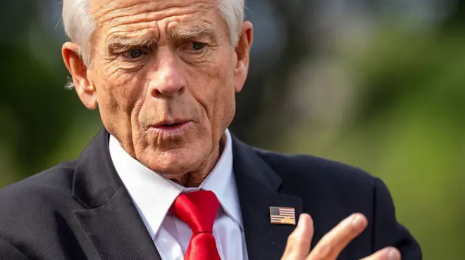 Peter Navarro, umujyanama mukuru ku bucuruzi n'inganda wo mu biro bya perezida w'Amerika (White House). Yambaye ikoti ry'umukara, ishati y'umweru na karuvati itukura. Arimo kuganira n'abanyamakuru i Washington DC, ku itariki ya 6 Kanama (8) mu mwaka wa 2025.