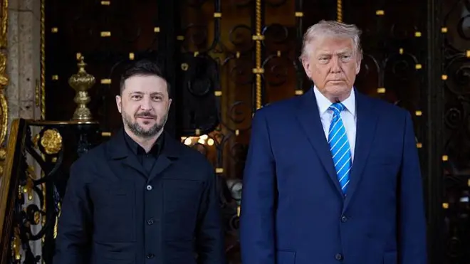 Зеленський і Трамп стоять поруч на сходах перед великою декоративною металевою брамою з позолоченими елементами. Ліворуч — людина в темному одязі без краватки, праворуч — вища людина в синьому костюмі з блакитною смугастою краваткою. Позаду видно оздоблені колони, ковані візерунки та вхід до розкішної будівлі.