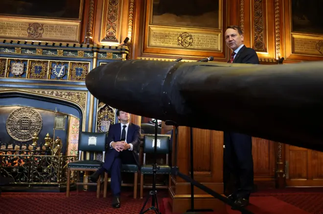 Polish foreign minister stands behind the nose cone of a Russian drone inside a wood-panelled room with a decorative fireplace