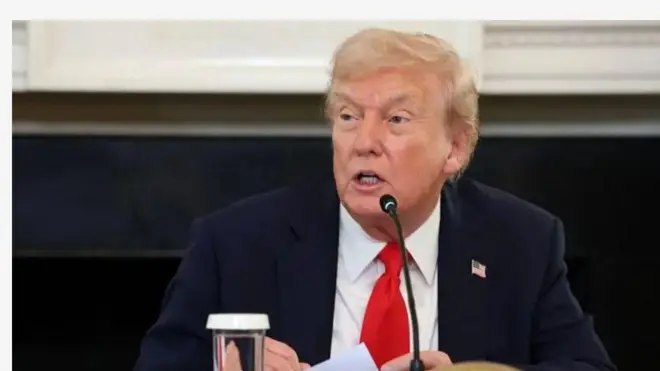 Aarẹ ilẹ America; Donald Trump n sọrọ ninu aworan yii. Ẹrọ gbohun-gbohun kan wa niwaju rẹ. Trump wọ aṣọ dudu, o wọ itẹnu alawọ funfun sinu, o si fi tai alawọ pupa le e.