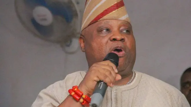 Gomina ipinlẹ Osun, Ademola Adeleke n sọrọ si ẹrọ gbohun-gbohun. O wọṣọ alawọ goolu, o de fila rẹ pẹlu. Ẹgba ọrun wa lọrun rẹ, o si fi ilẹkẹ meji sọwọ.