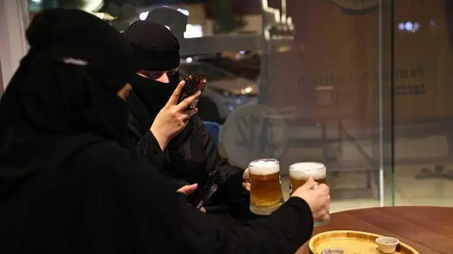 Saudi women take photographs of their non-alcoholic draft beer at the A12 cafe in the capital Riyadh on October 24, 2025. Draft beer, peanuts and big-screen sports... the scene is reminiscent of pubs worldwide, but in Riyadh customers in white robes or black veils sip non-alcoholic pints, with no expectation of a hangover.