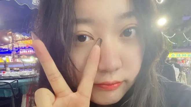 Miss Zhu holding her figers woth long black finger nails up in a V pattern
