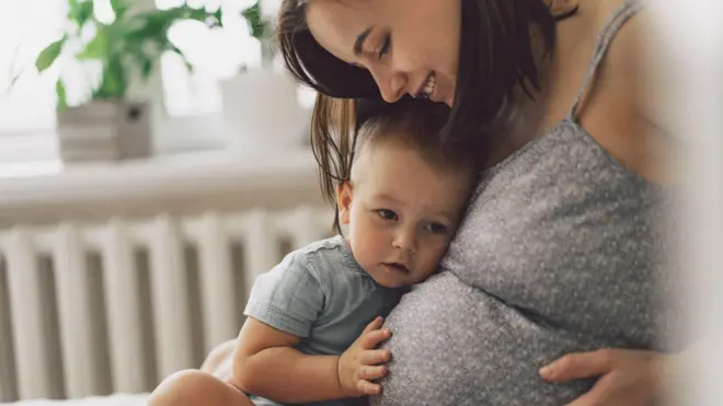 Niño escucha el estomago de su madre embarazada. 