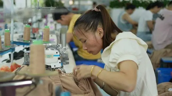 Makine başında dikiş diken tekstil işçisi bir kadın ve diğer işçiler