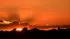 ロンドンの、ドラマチックで鮮やかなオレンジ色の夕焼け空。シルエットになった木々の上から光る夕日が雲間にのぞいている
