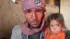 Un hombre que lleva un turbante rosa abraza estrechamente a su pequeña hija frente a una pared de barro agrietada.
