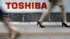 Pedestrians walk past a logo of Toshiba Corp outside an electronics retailer in Tokyo.