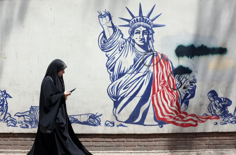 امرأة تسير بجوار جدارية مناهضة للولايات المتحدة بجوار السفارة الأمريكية السابقة في طهران