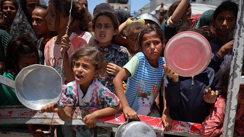 Ƙananan yara riƙe da faranti suna jiran a raba musu abinci a Gaza