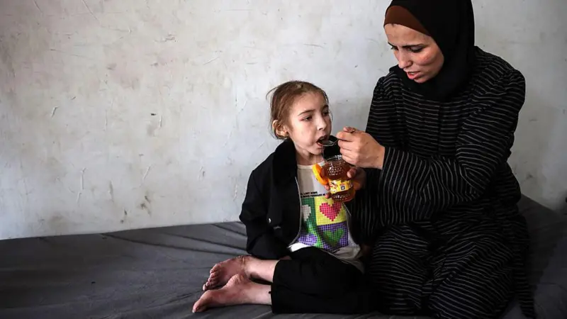 Shuruq attempts to comfort her daughter Rafah, 12, who suffers from malnutrition.