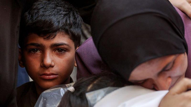 Bir kadın bir kefene sarılırken yanında da gözü yaşlı bir çocuk kemaraya bakıyor