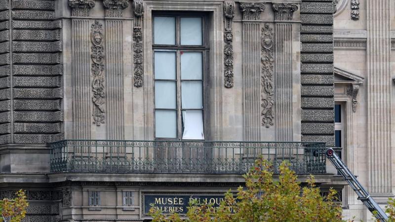 Над вывеской музея Лувр балкон со стеклянной дверью, одно из стекол повреждено, к балкону сбоку приставлена лестница