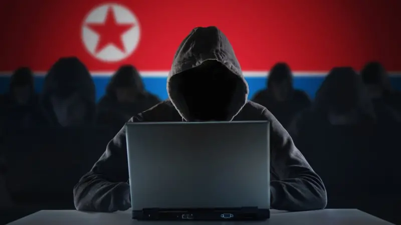 북한 국기를 배경으로 노트북을 사용하는 후드 쓴 인물
