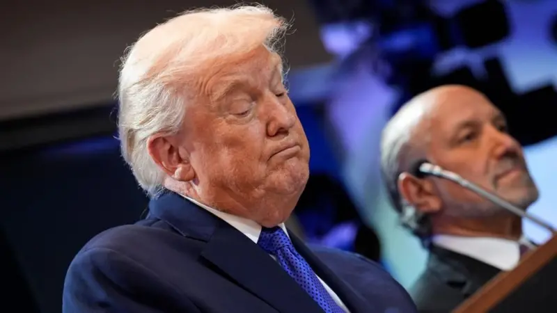 スーツ姿のトランプ氏が演壇に立ち、下を向いて資料を読んでいるような表情をしている