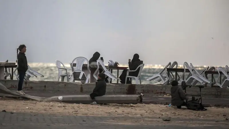 أطفال ونساء يقضون أوقاتهم، بعضهم جالس على كراسي بلاستيكية، على شاطئ البحر الأبيض المتوسط ​​في مدينة غزة، في 16 ديسمبر/كانون الأول 2025