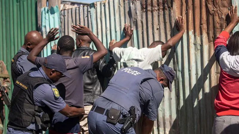 Police arrest gangs for Cape Town on 13 April 2026. Di men raise dia hands while police try to hold dem.