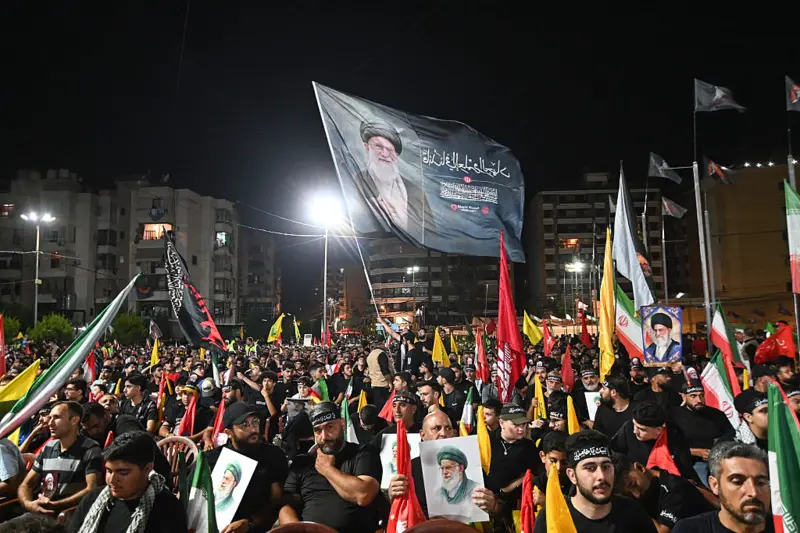 مئات الشبان باللباس الأسود ورايات حزب الله يجلسون وفي المقدمة بعضهم يرفع صور علي خامنئي