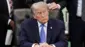 米大統領執務室で机に向かって座り、両手を組んだトランプ氏が、口を閉じ、左の方を見ている。ダークスーツに青いネクタイを着けている