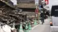 車道沿いの家屋が地震で倒壊しており、緑色のコーンで封鎖されている。その横を車や自転車が走っている
