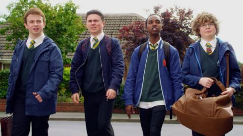 Four boys in school uniform walking down a suburban street.