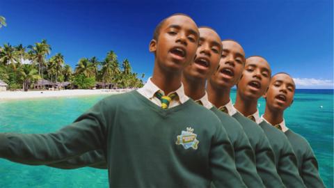 A boy in a school uniform standing next to a picture of a desert island, Nero.